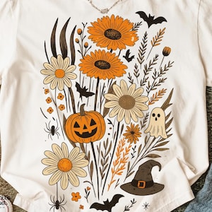 Peut inclure: T-shirt cr&egrave;me avec un motif floral d'Halloween. Le graphisme comprend des tournesols orange, des marguerites, une citrouille sculpt&eacute;e, des chauves-souris, un fant&ocirc;me et un chapeau de sorci&egrave;re. Le t-shirt porte l'inscription "Comfort Colors".