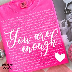 May include: A bright pink sweatshirt with the words "You are enough" in white script. The text is surrounded by a longer inspirational message. A disco ball and a magazine are in the background.