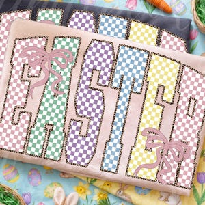 May include: Three pastel-colored t-shirts with the word "EASTER" printed on them. The letters are checkered in pink, green, purple, blue, and yellow, with a leopard print outline. Each shirt has a pink bow. Easter-themed apparel.