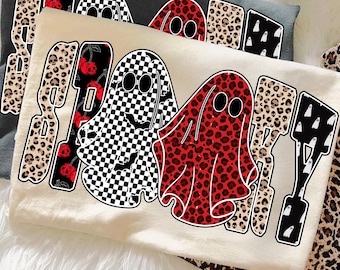 May include: Three t-shirts with a Halloween theme. The central shirt is cream-colored, featuring two ghost figures, one checkered and one red leopard print. The word "SPOOKY" is printed above the ghosts in a mix of leopard print, cherries, and skull designs.