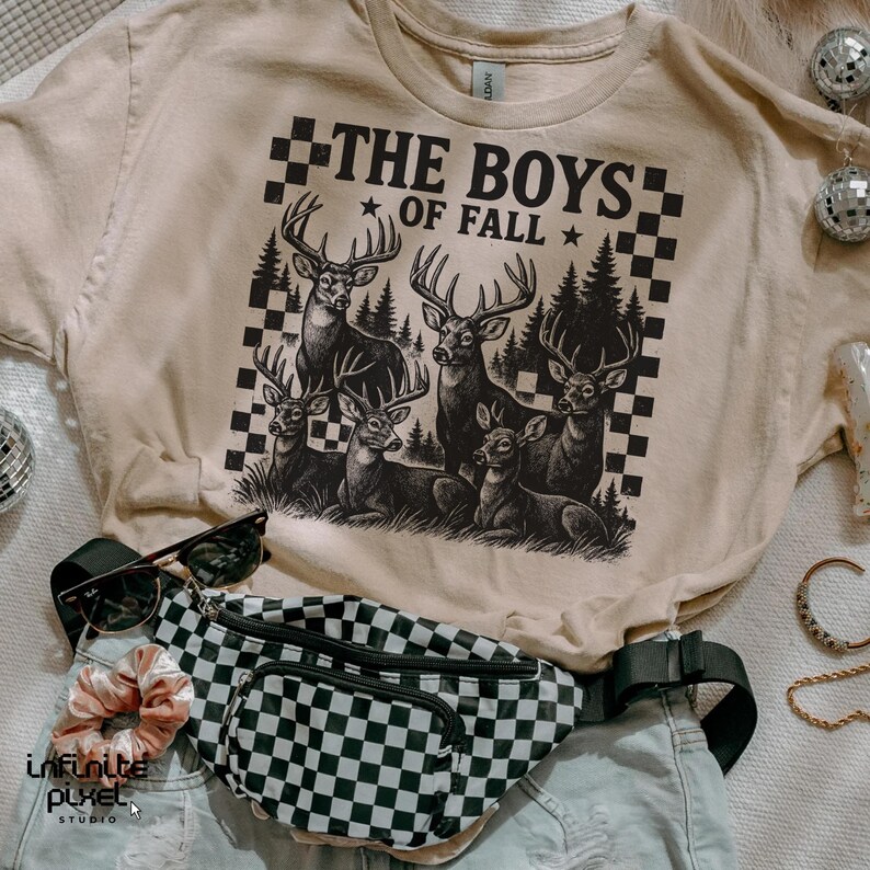 May include: Beige t-shirt with a graphic of deer and the text "THE BOYS OF FALL". A black and white checkered fanny pack, sunglasses, and a scrunchie are also visible.