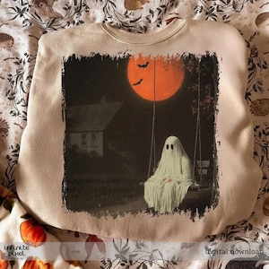 May include: Beige sweatshirt featuring a spooky Halloween design. The graphic depicts a ghost sitting on a swing under an orange moon with bats. A house is in the background. The words "digital download" are at the bottom.