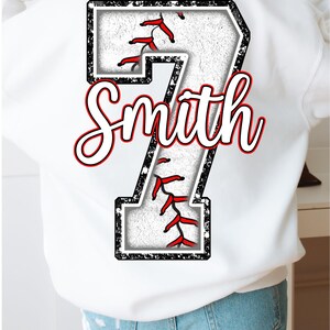 Pu&ograve; includere: Felpa bianca con un numero 7 nero e bianco a tema baseball con cuciture rosse. Il nome "Smith" &egrave; scritto in corsivo bianco sopra il numero.