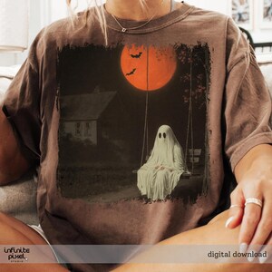 May include: Brown t-shirt featuring a spooky Halloween design. The graphic depicts a ghost on a swing set under a large orange moon with bats. A house is in the background. The words "digital download" are at the bottom.