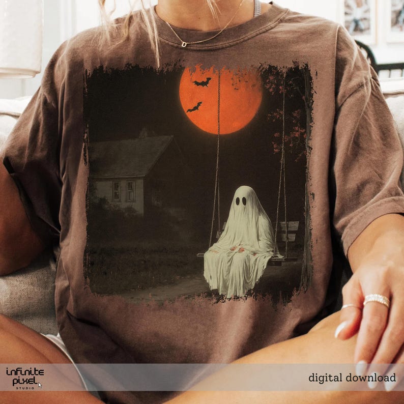 May include: Brown t-shirt featuring a spooky Halloween design. The graphic depicts a ghost on a swing set under a large orange moon with bats. A house is in the background. The words "digital download" are at the bottom.