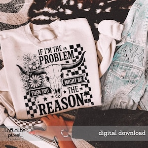 May include: Cream-colored sweatshirt with a graphic design featuring a bull skull, flowers, and the text "IF I'M THE PROBLEM THEN YOU MIGHT BE THE REASON." The design is in black and white, with a checkered pattern. A denim jacket is visible.