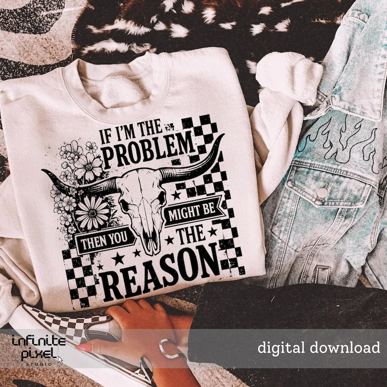 May include: Cream-colored sweatshirt with a graphic design featuring a bull skull, flowers, and the text "IF I'M THE PROBLEM THEN YOU MIGHT BE THE REASON." The design is in black and white, with a checkered pattern. A denim jacket is visible.