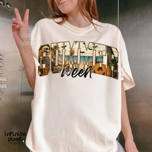 May include: Cream-colored t-shirt with a graphic that reads "Summerween." The design incorporates a skeleton, beach scene, palm trees, and pumpkins. The shirt has short sleeves and a relaxed fit.