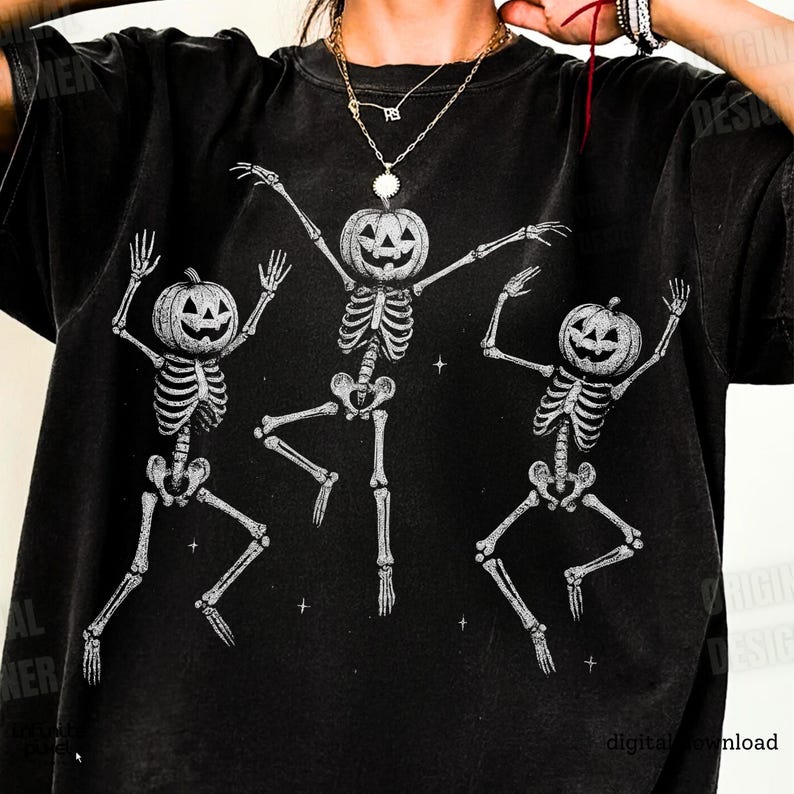 May include: Black t-shirt featuring a Halloween design with three dancing skeletons. Each skeleton has a carved pumpkin for a head and is in a playful pose. The design is in white, creating a contrast against the dark fabric.