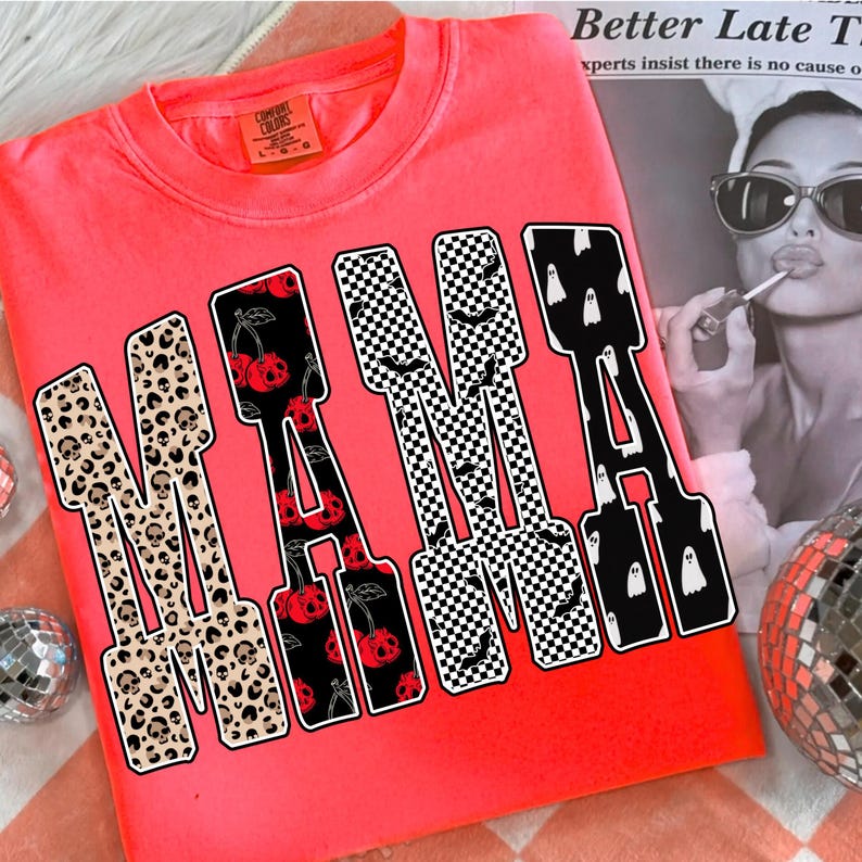 May include: A neon pink sweatshirt with the word "MAMA" in a bold, block letter design. The letters feature various patterns, including leopard print with skulls, cherries, checkered patterns with bats, and white ghosts.
