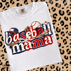May include: White t-shirt with a baseball-themed graphic. The design features the words "Baseball Mama" in red and blue, along with baseballs, a bat, and a baseball cap. The shirt has a crew neck and short sleeves.