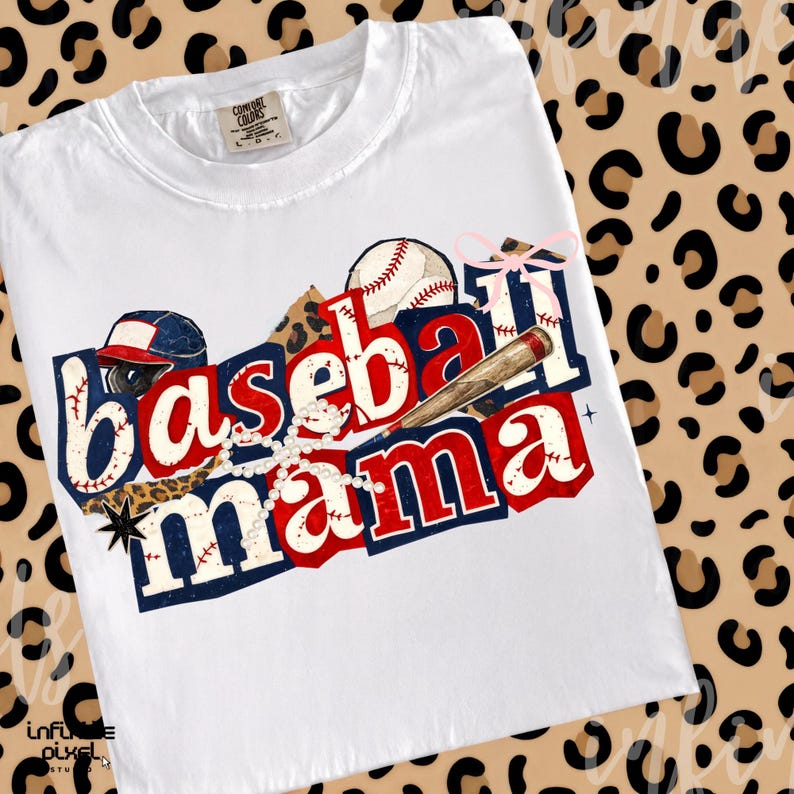 May include: White t-shirt with a baseball-themed graphic. The design features the words "Baseball Mama" in red and blue, along with baseballs, a bat, and a baseball cap. The shirt has a crew neck and short sleeves.