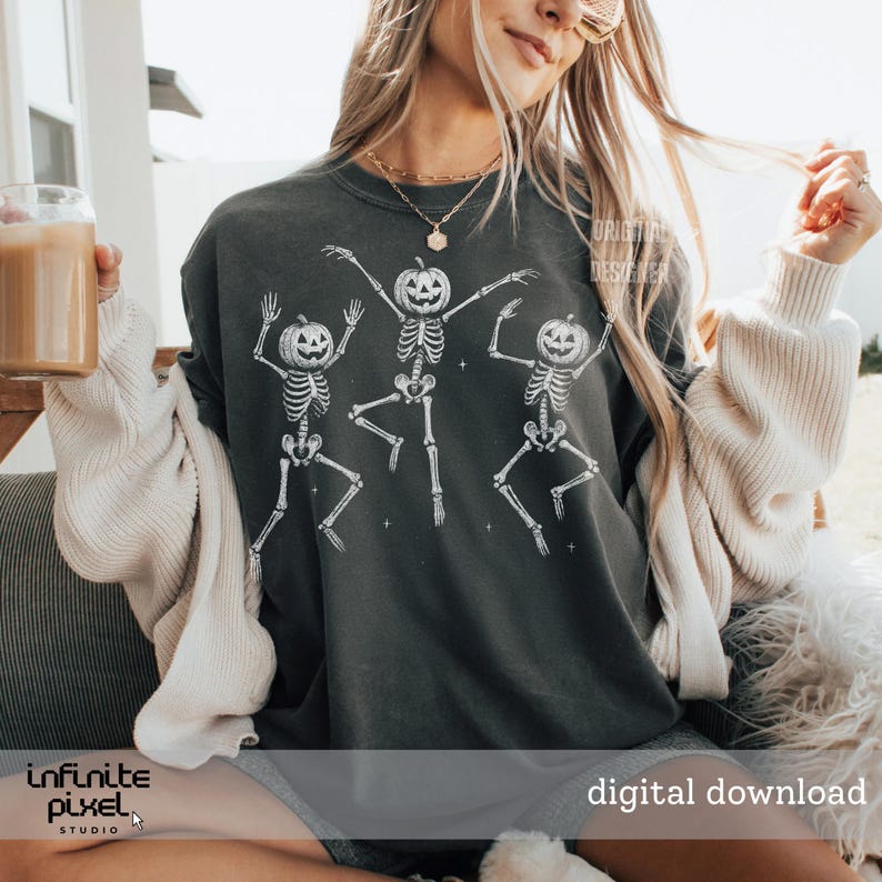 May include: Dark gray sweatshirt featuring a white graphic of three dancing skeletons with pumpkin heads. The phrase "digital download" is visible in the lower right corner. The sweatshirt is part of a Halloween-themed collection.