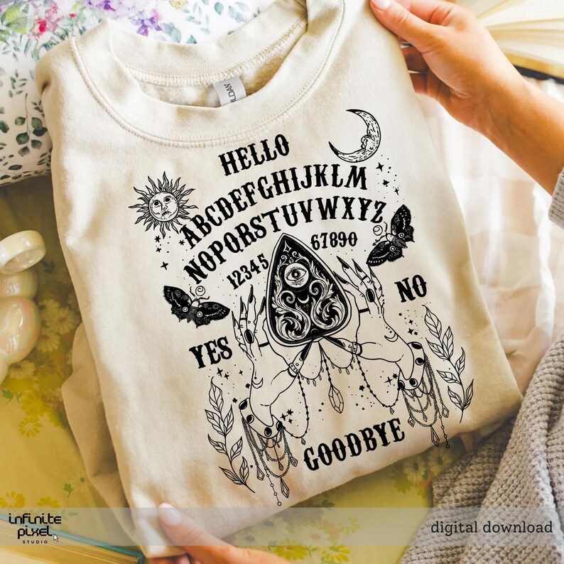 May include: Cream-coloured sweatshirt with a black Ouija board design. The design includes the alphabet, numbers, sun, moon, butterflies, and the words "Hello", "Yes", "No", and "Goodbye". The design features hands holding a planchette.