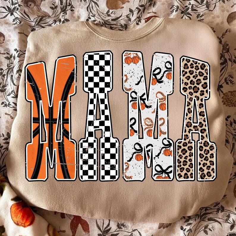 Puede incluir: Una sudadera beige con la palabra "MAMA" en letras grandes y audaces. La "M" es naranja con un dise&ntilde;o de baloncesto, la "A" es a cuadros blancos y negros, la segunda "M" es blanca con balones de baloncesto y cintas, y la &uacute;ltima "A" es estampado de leopardo.