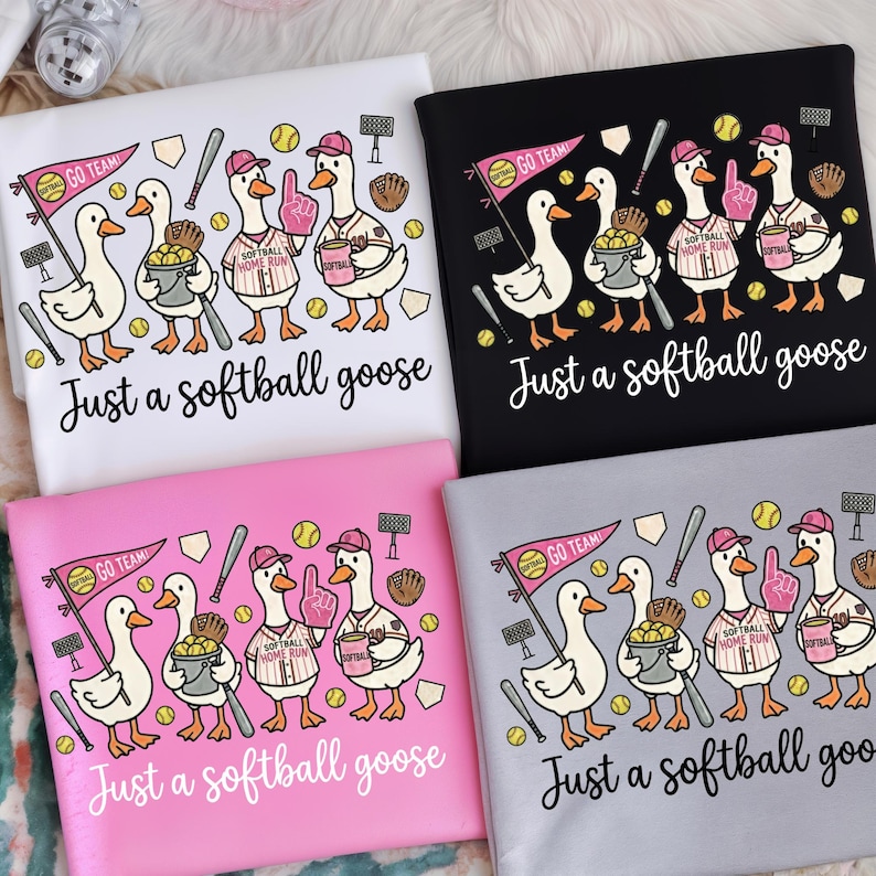 May include: Four t-shirts with a softball theme. Each shirt features a cartoon goose wearing a baseball cap and holding softball-related items. The text "Just a softball goose" is printed below the graphic. The shirts are in white, black, pink, and gray.