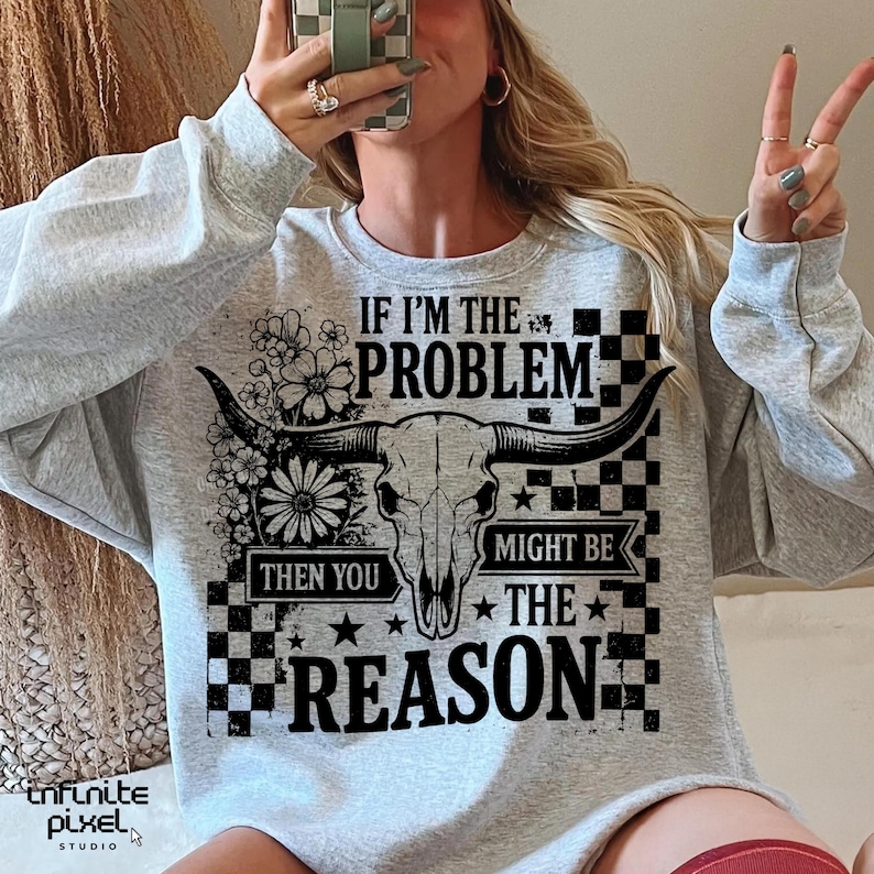 May include: A light gray sweatshirt with a graphic design featuring a bull skull, flowers, and the text "IF I'M THE PROBLEM THEN YOU MIGHT BE THE REASON". The design includes black and white checkered patterns and stars.