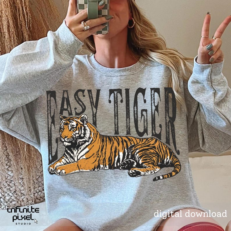 May include: A grey sweatshirt featuring the words "EASY TIGER" above a tiger illustration. The tiger is orange and black. The words "digital download" are at the bottom right.