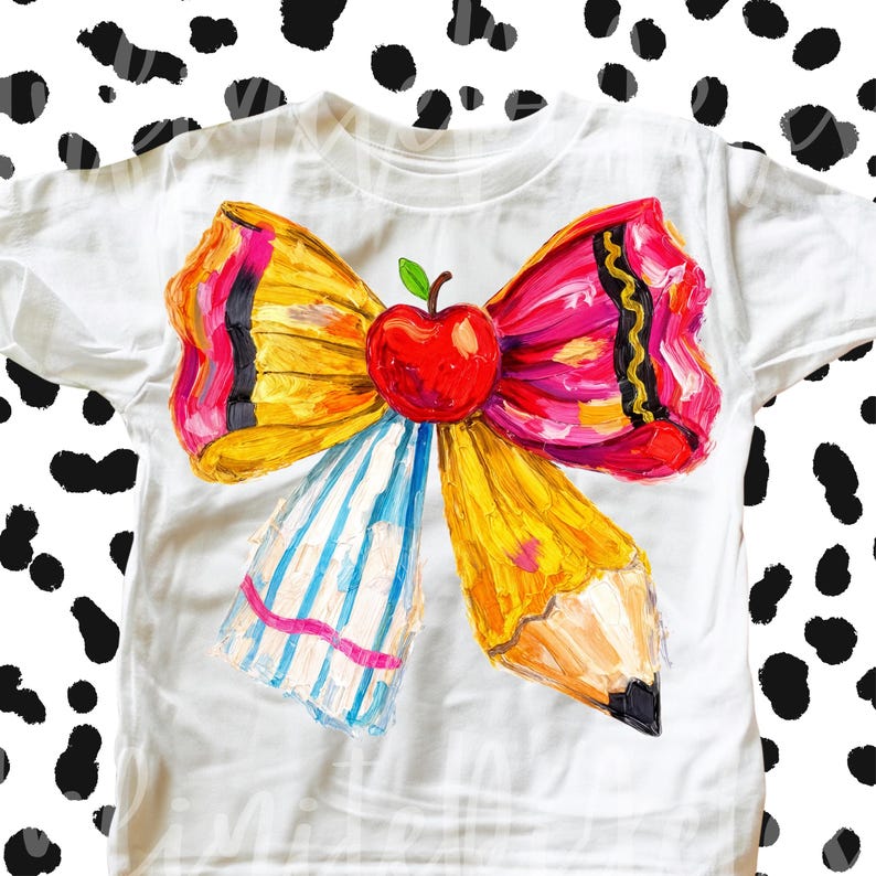 May include: White t-shirt featuring a colorful bow design with a red apple in the center. The bow is made of a yellow pencil and pink and yellow ribbons. The shirt is a school-themed design.