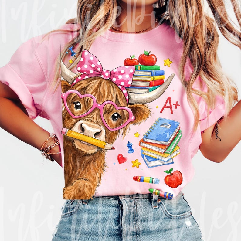 Pu&ograve; includere: T-shirt rosa con un cartone animato di una mucca delle Highlands con occhiali a forma di cuore e un fiocco a pois. La mucca tiene una matita, circondata da libri, mele e materiale scolastico. La maglietta ha la scritta "A+".