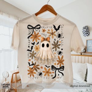 May include: Cream t-shirt with a ghost design, orange flowers, spiders, and bats. The shirt has the text "digital download". The shirt is hanging on a wooden hanger. The design includes a bow on the ghost and black bows.