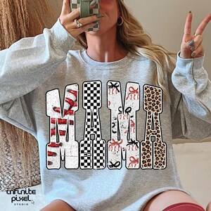 May include: A light grey sweatshirt featuring the word "MAMA" in a large, decorative font. The letters are filled with patterns like red and white candy canes, a black and white checkerboard, red bows, and a leopard print design.