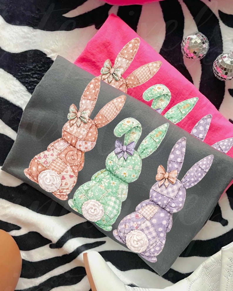 May include: Three decorative pillows with patchwork bunny designs in shades of pink, gray, and green. Each bunny has a bow and a floral or polka dot pattern. The pillows are on a zebra-striped surface.