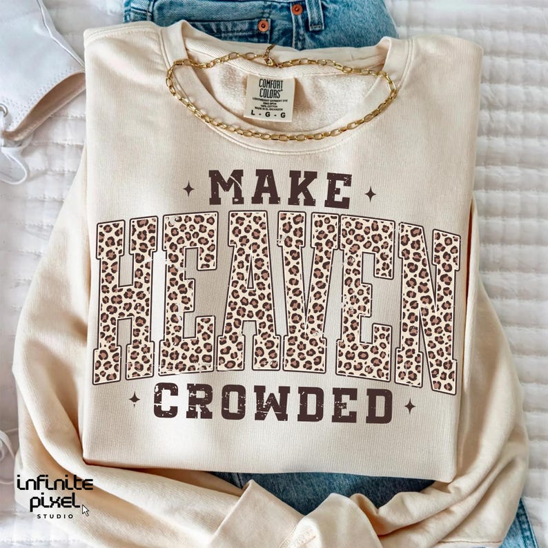 May include: A cream-colored sweatshirt with the text "MAKE HEAVEN CROWDED" in brown. The word "HEAVEN" is filled with a leopard print pattern. A gold chain necklace is draped across the top of the sweatshirt.