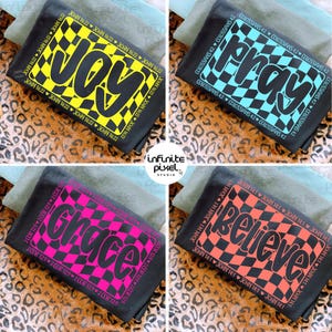 May include: Four black t-shirts with different words in a checkered design. The words are "Joy" in yellow, "Pray" in blue, "Grace" in pink, and "Believe" in orange. Each shirt has a Bible verse printed around the word.