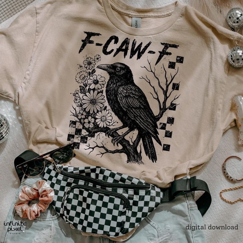 Puede incluir: Camiseta beige con un gr&aacute;fico negro de un cuervo posado en una rama, rodeado de flores y el texto "F-CAW-F". Tambi&eacute;n se ve una ri&ntilde;onera a cuadros en blanco y negro, gafas de sol y una goma para el pelo.