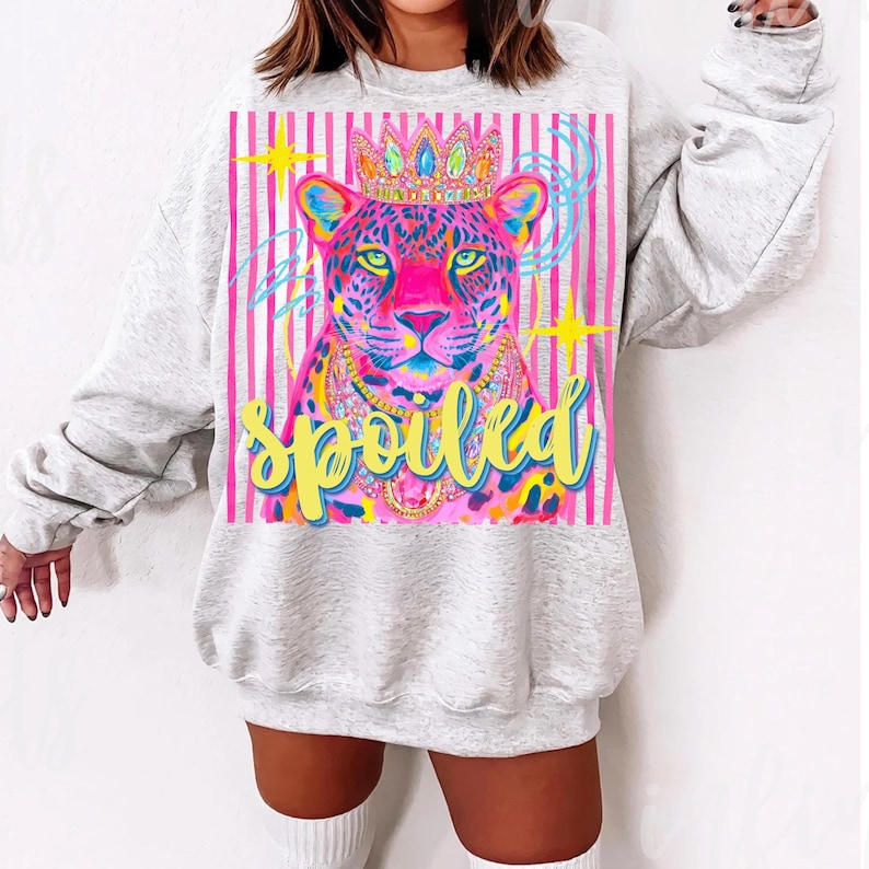 May include: A light gray sweatshirt featuring a colorful leopard illustration wearing a crown and necklace. The leopard is set against a pink striped background with the word "Spoiled" in yellow script.
