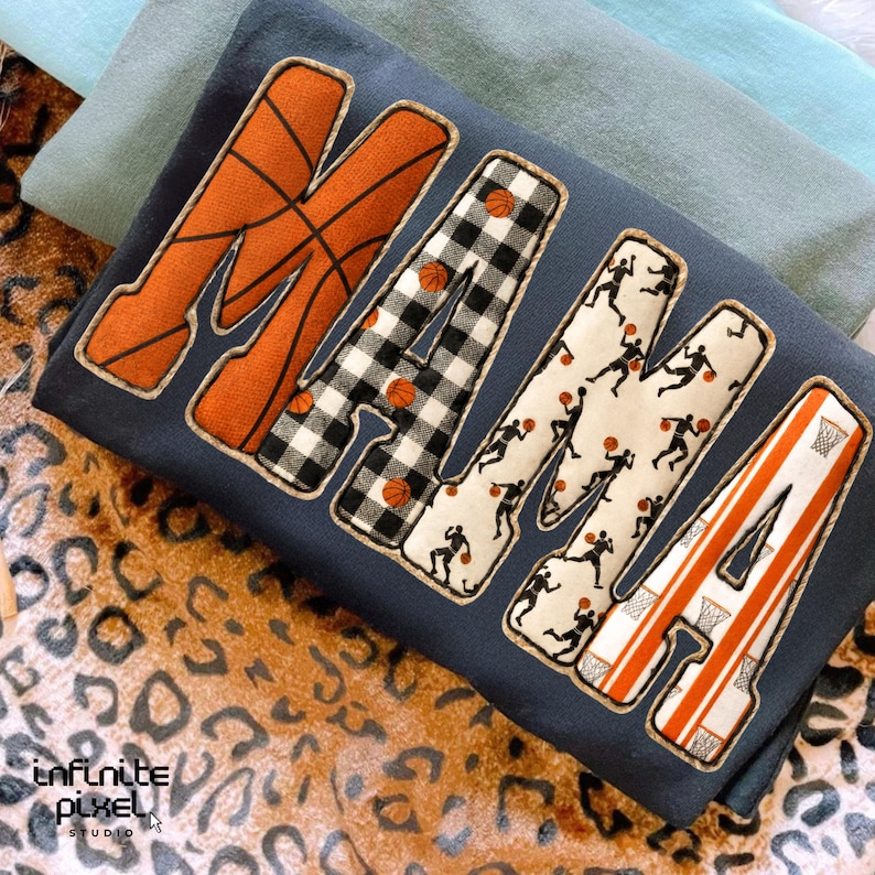 Puede incluir: Sudadera azul marino con la palabra "MAMA" en letras grandes y decorativas. La "M" es naranja con un dise&ntilde;o de baloncesto, la primera "A" es a cuadros blancos y negros, la segunda "M" tiene siluetas de jugadores de baloncesto.