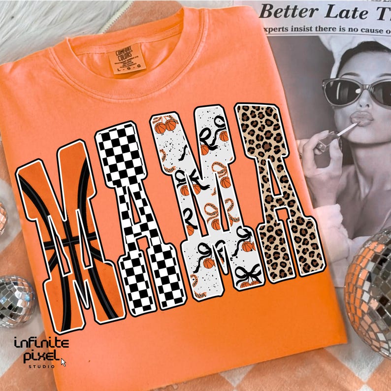 Puede incluir: Sudadera naranja con cuello redondo con la palabra "MAMA" en letras grandes y decorativas. Las letras presentan patrones tem&aacute;ticos de baloncesto, incluyendo balones de baloncesto, patrones de cuadros y estampado de leopardo. La camisa tiene una etiqueta Comfort Colors.