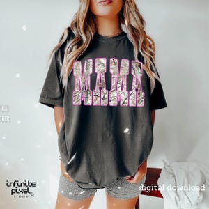 May include: Dark gray t-shirt with the word "MAMA" in a camouflage design with pink outlines. The shirt is a relaxed fit and has short sleeves. The image also includes the text "digital download".