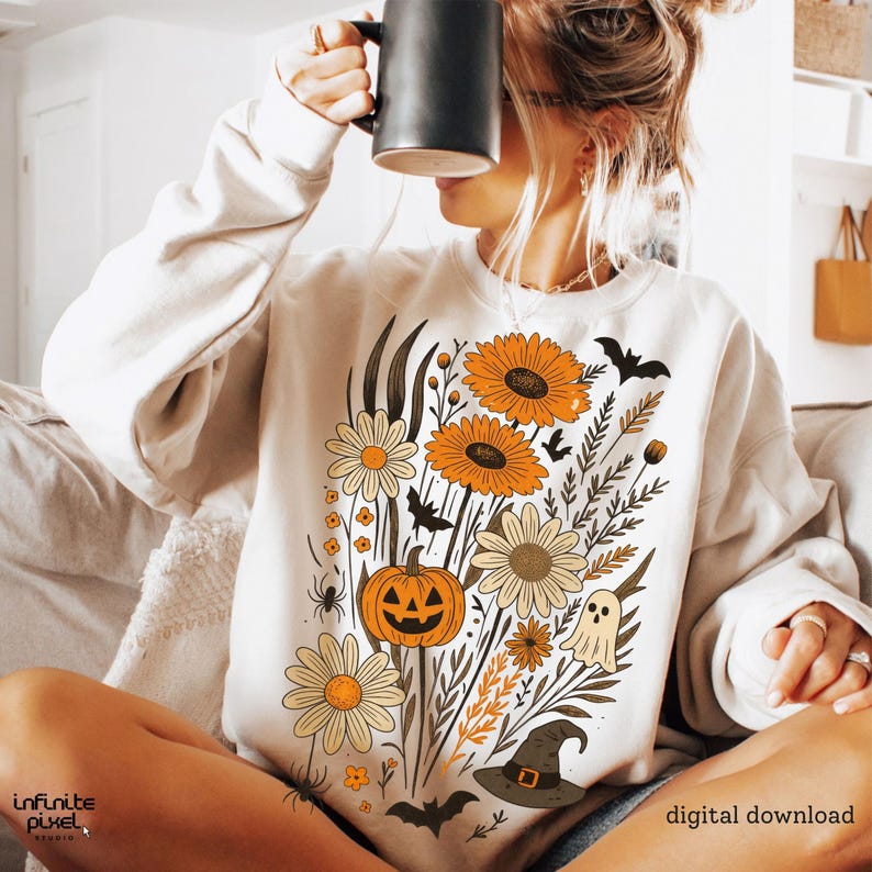Peut inclure: Sweat-shirt cr&egrave;me avec un motif floral d'Halloween. Il pr&eacute;sente des tournesols orange, une citrouille, des chauves-souris et un chapeau de sorci&egrave;re. Les mots "digital download" sont imprim&eacute;s en bas &agrave; droite.