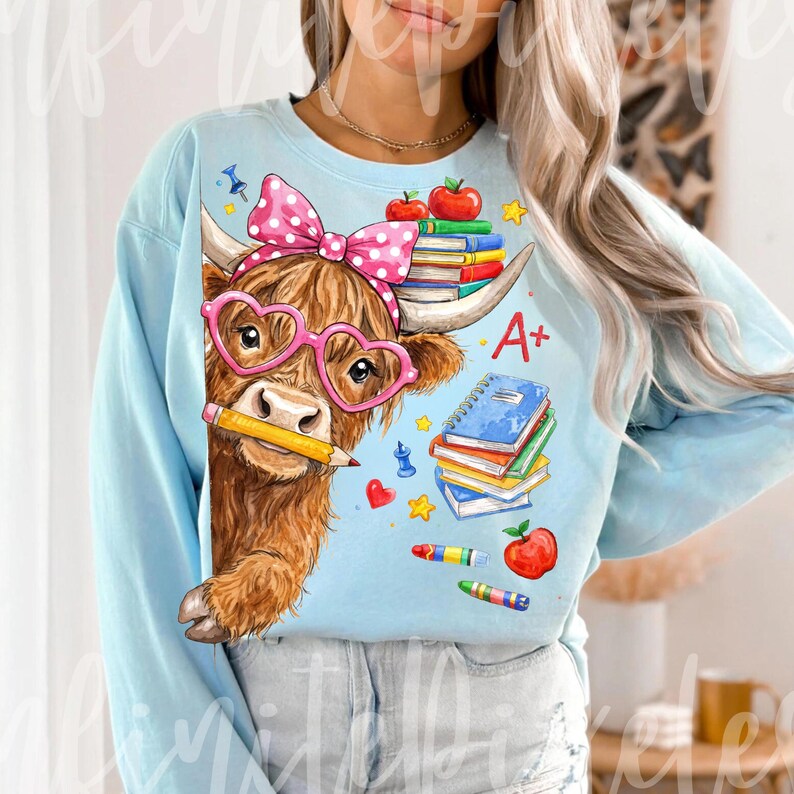 Pu&ograve; includere: Felpa azzurra con una mucca delle Highlands marrone che indossa occhiali rosa a forma di cuore e un fiocco a pois. La mucca tiene in mano una matita ed &egrave; circondata da elementi grafici a tema scolastico, tra cui libri, mele e la scritta "A+".