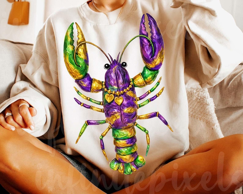 May include: Cream-colored sweatshirt featuring a vibrant, detailed illustration of a Mardi Gras lobster. The lobster is adorned with purple, green, and gold accents, and a heart-shaped necklace. The design is centered on the front of the shirt.