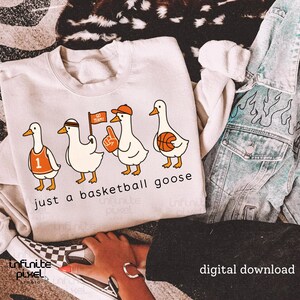 May include: A cream-coloured sweatshirt with a cartoon design of four geese dressed as basketball players. The text "just a basketball goose" is printed below the geese. The geese are wearing basketball-themed accessories.