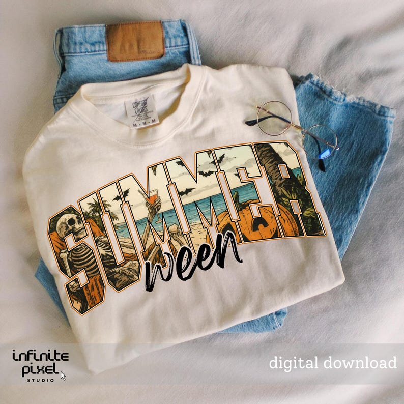 May include: Cream-colored t-shirt with the word "SUMMERween" in a beach-themed graphic. The design includes skeletons, pumpkins, palm trees, and bats. The shirt is laid on top of blue jeans, with a pair of glasses resting on the shirt.
