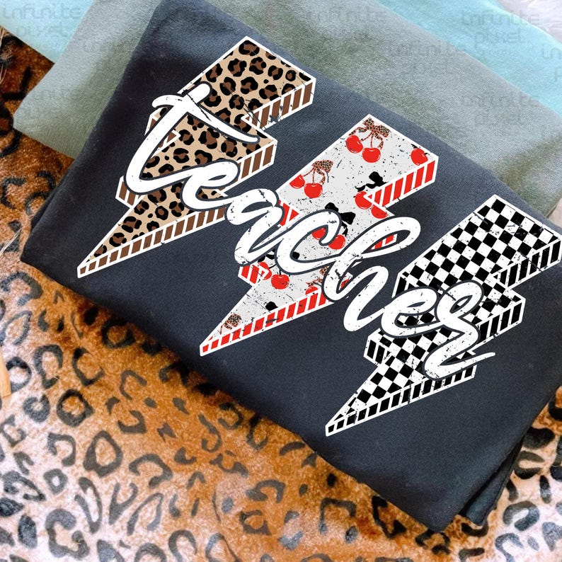 May include: Black t-shirt with the word "Teaches" in a lightning bolt design. The lightning bolts feature leopard print, cherries, and a black and white checkered pattern. The shirt is folded on a leopard print surface.