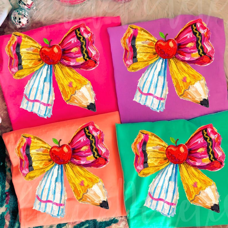 May include: Four colorful t-shirts, each featuring a unique design. The design is a pencil-shaped bow with a red apple in the center. The shirts are in pink, purple, orange, and green.