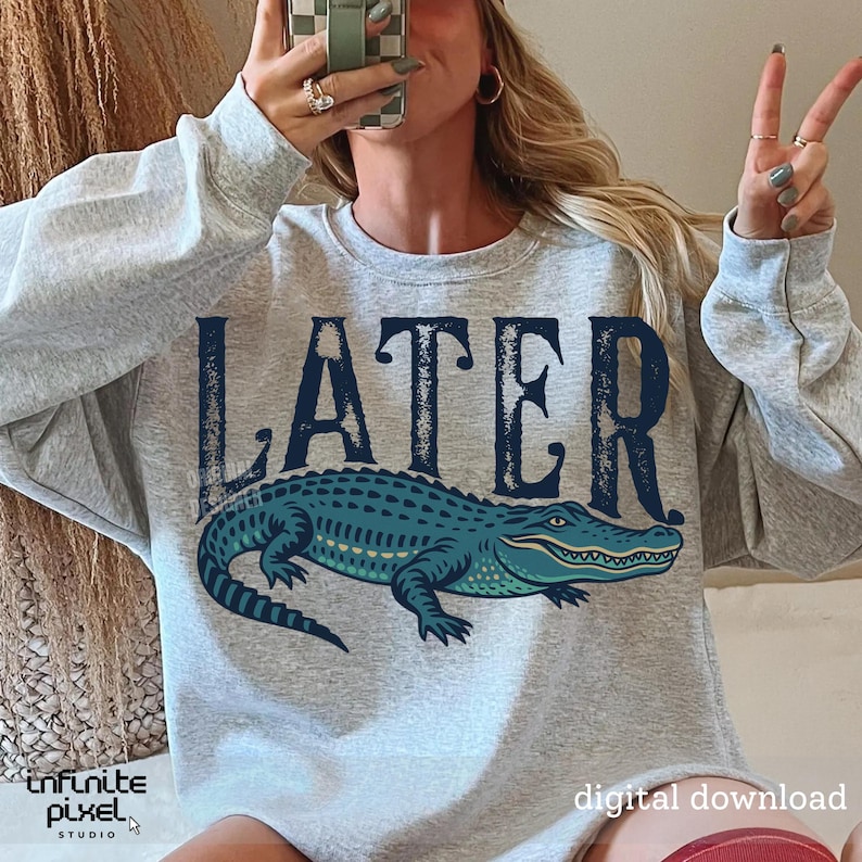 Pode incluir: Camisola cinzenta com a palavra "LATER" impressa em preto e um gr&aacute;fico de um jacar&eacute; azul.