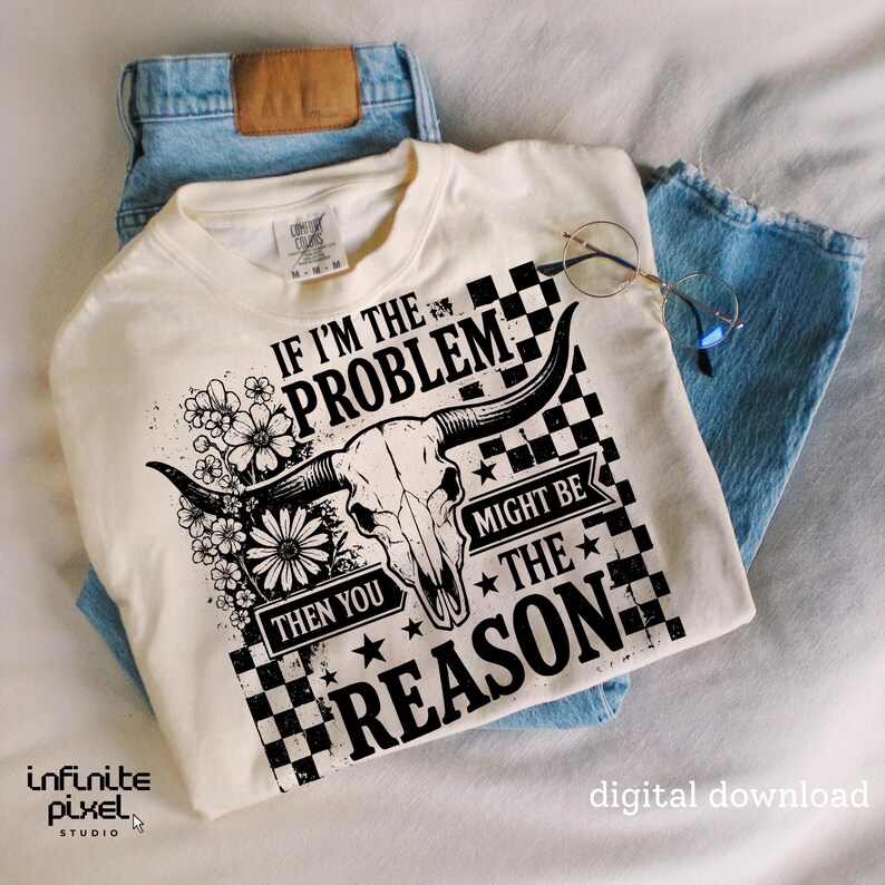 May include: Cream-colored t-shirt with a graphic featuring a bull skull, flowers, and the text "IF I'M THE PROBLEM THEN YOU MIGHT BE THE REASON." The shirt is paired with light blue jeans and round glasses.