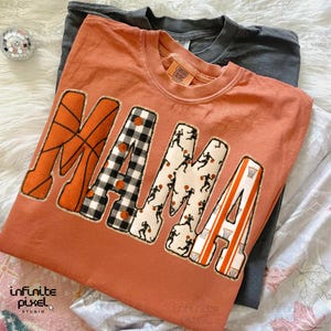 Puede incluir: Una camiseta de color naranja quemado con la palabra "MAMA" en un tema de baloncesto. La "M" es naranja con l&iacute;neas de baloncesto, la "A" es a cuadros blancos y negros, la segunda "M" tiene siluetas de jugadores de baloncesto y la "A" final tiene rayas naranjas y blancas.