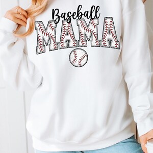 Pu&ograve; includere: Felpa bianca con il testo "Baseball Mama" in lettere nere con un design a punto di baseball rosso. Sotto il testo c'&egrave; una palla da baseball rossa con cuciture bianche.