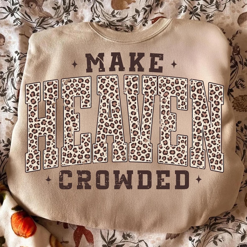 May include: A beige sweatshirt with the text "MAKE HEAVEN CROWDED" in a brown, leopard print font. The sweatshirt has a crew neck and long sleeves. The text is centered on the front of the shirt.