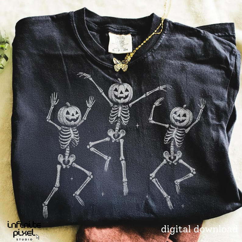 May include: Black t-shirt featuring a graphic of three dancing skeletons with pumpkin heads. The skeletons are in a playful pose, with their arms raised. A gold butterfly necklace is draped on the shirt. The words "digital download" are at the bottom.