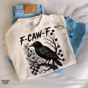 Puede incluir: Camiseta color crema con una ilustraci&oacute;n de cuervo negro, el texto "F-CAW-F" y detalles florales. La camiseta se combina con vaqueros azules y gafas redondas. El dise&ntilde;o incluye un patr&oacute;n de cuadros y ramas de &aacute;rboles desnudas.
