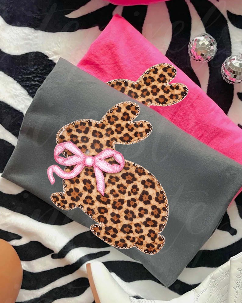 May include: Two decorative pillows, one grey and one pink, with a leopard print bunny design. The bunny has a pink bow. The pillows are on a zebra-striped surface with disco balls.