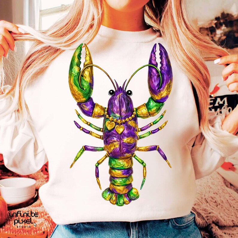 May include: White sweatshirt featuring a colorful illustration of a lobster. The lobster design incorporates purple, green, and gold accents, with heart-shaped details on a necklace. The design is vibrant and eye-catching.